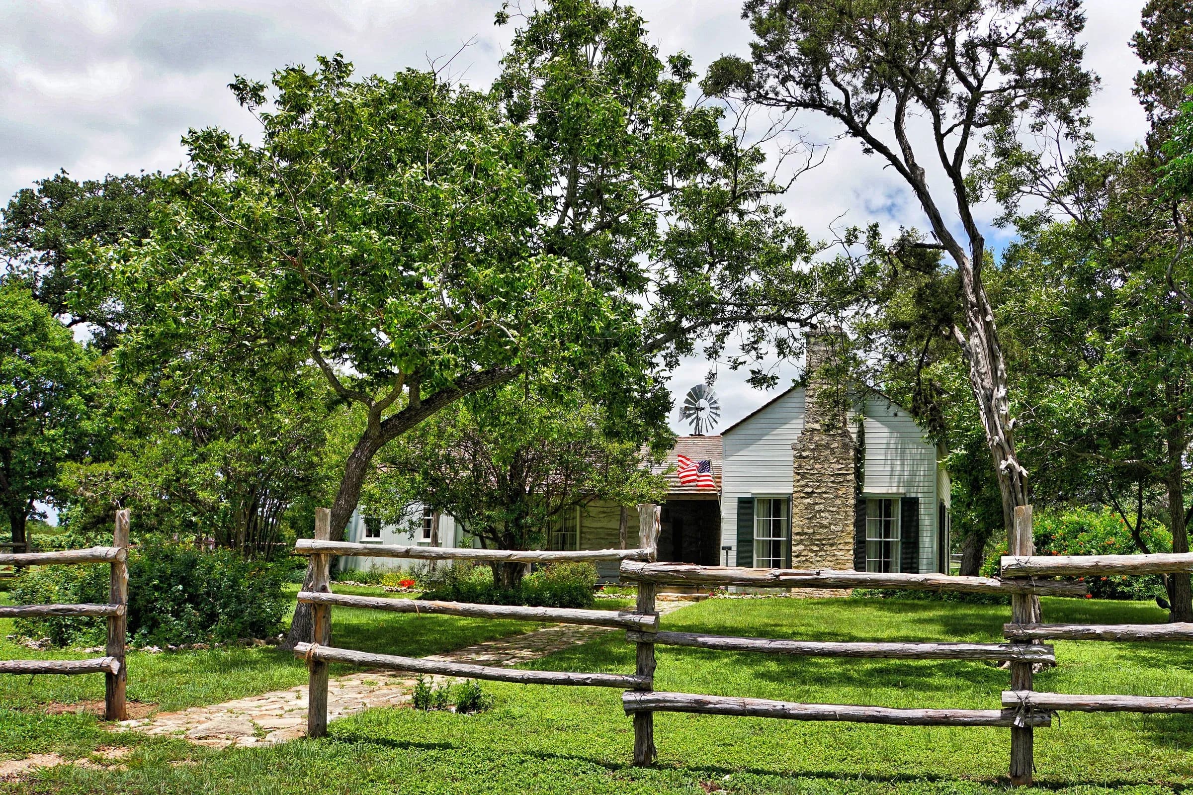 The 1850s Pound farmstead house, now a museum, behind a split-rail cedar fence under live oaks in Dripping Springs, Texas