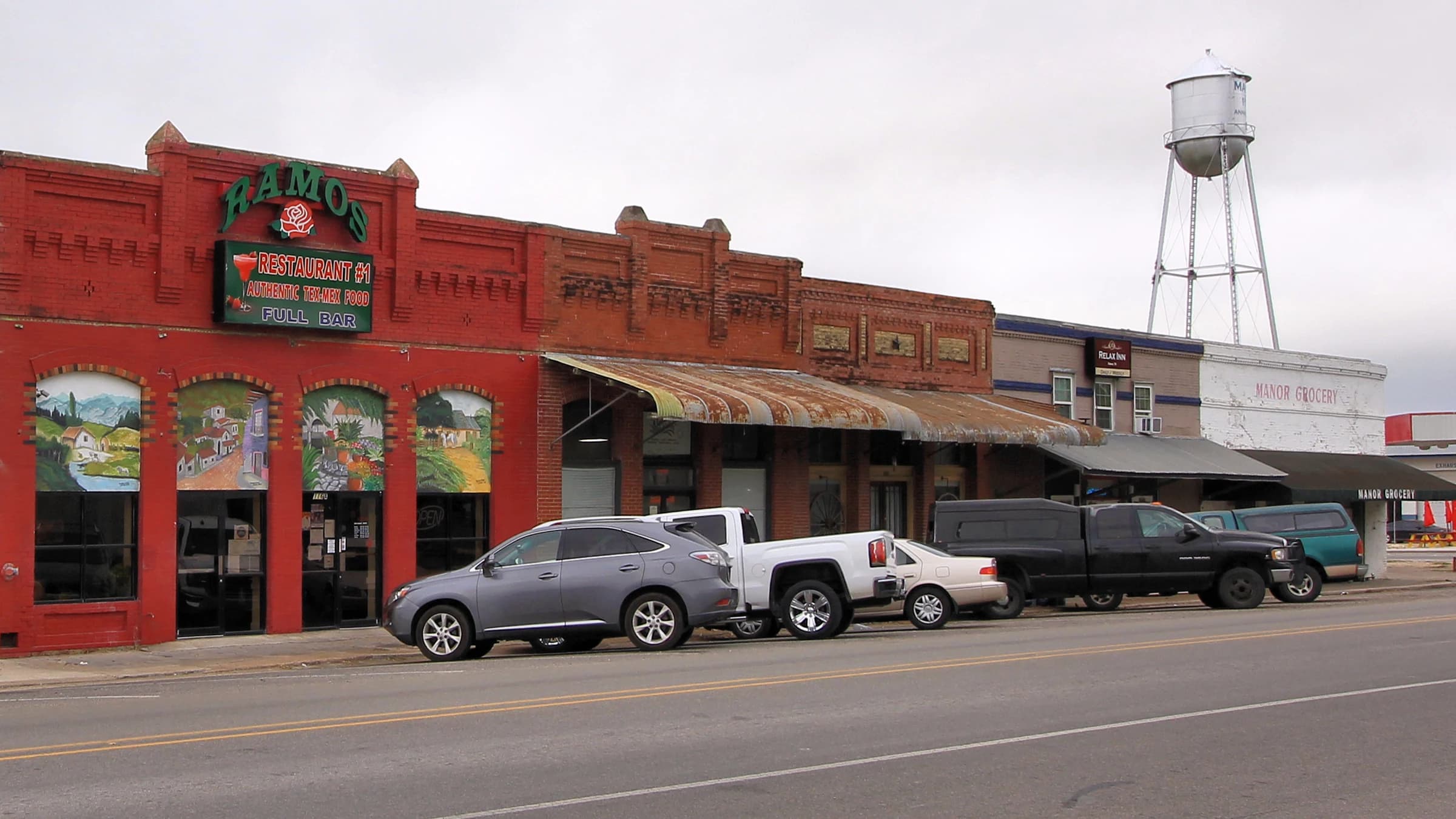 Old red-brick commercial buildings on the main street of downtown Manor, Texas, with the town's 1930s water tower rising behind them