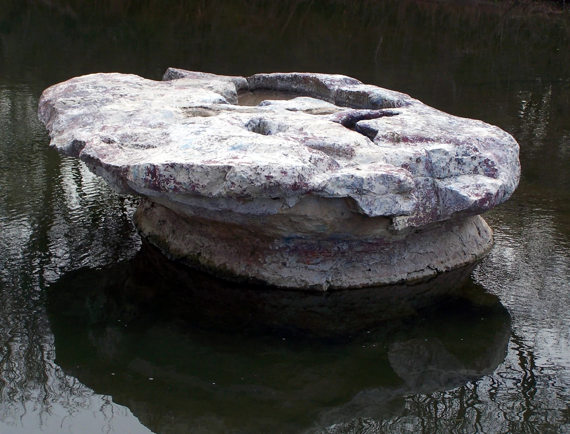 The table-shaped limestone Round Rock sitting in Brushy Creek, the old wagon-crossing landmark that gave Round Rock, Texas its name, reflected in dark water