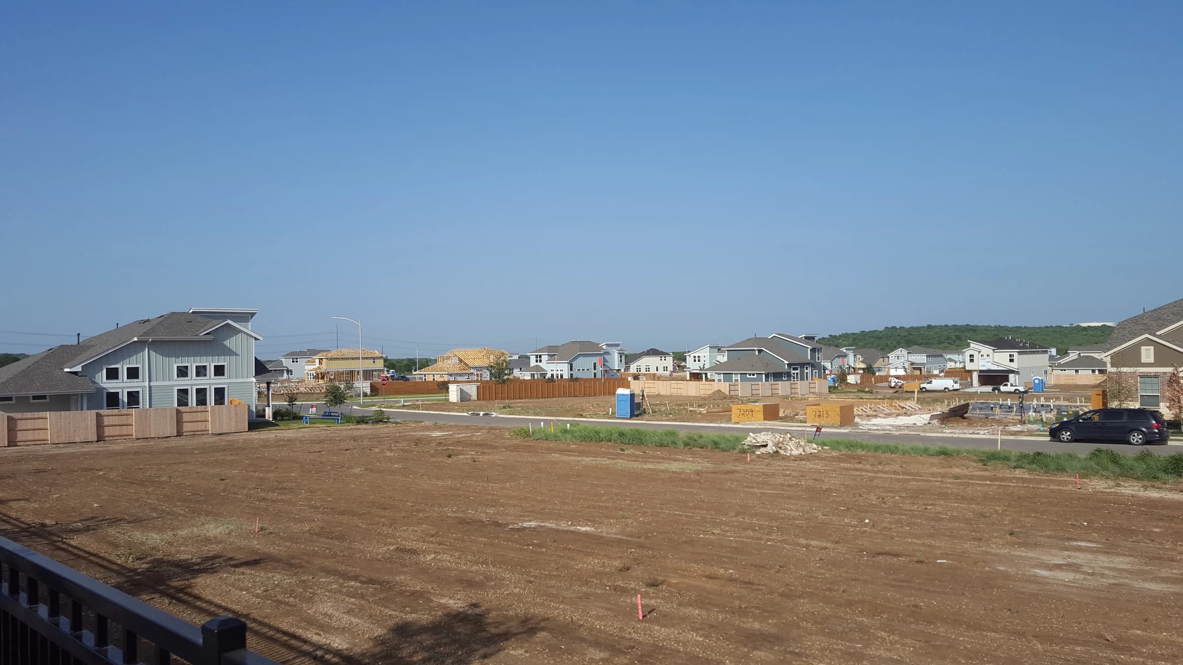 New gray and blue two-story houses along a freshly paved Easton Park street in southeast Austin in 2016, with framing going up and bare lots waiting for foundations