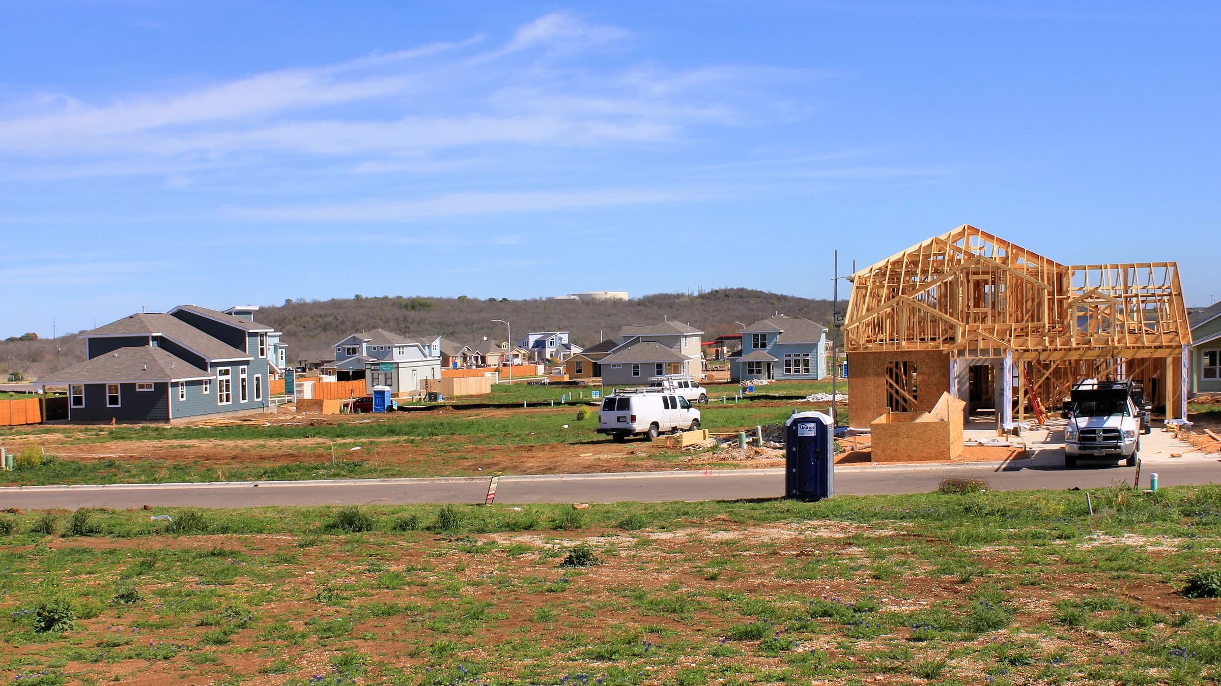 New two-story houses and a timber-framed house going up on a curbed street in Easton Park, southeast Austin, in 2016, with the wooded rise of Pilot Knob on the horizon