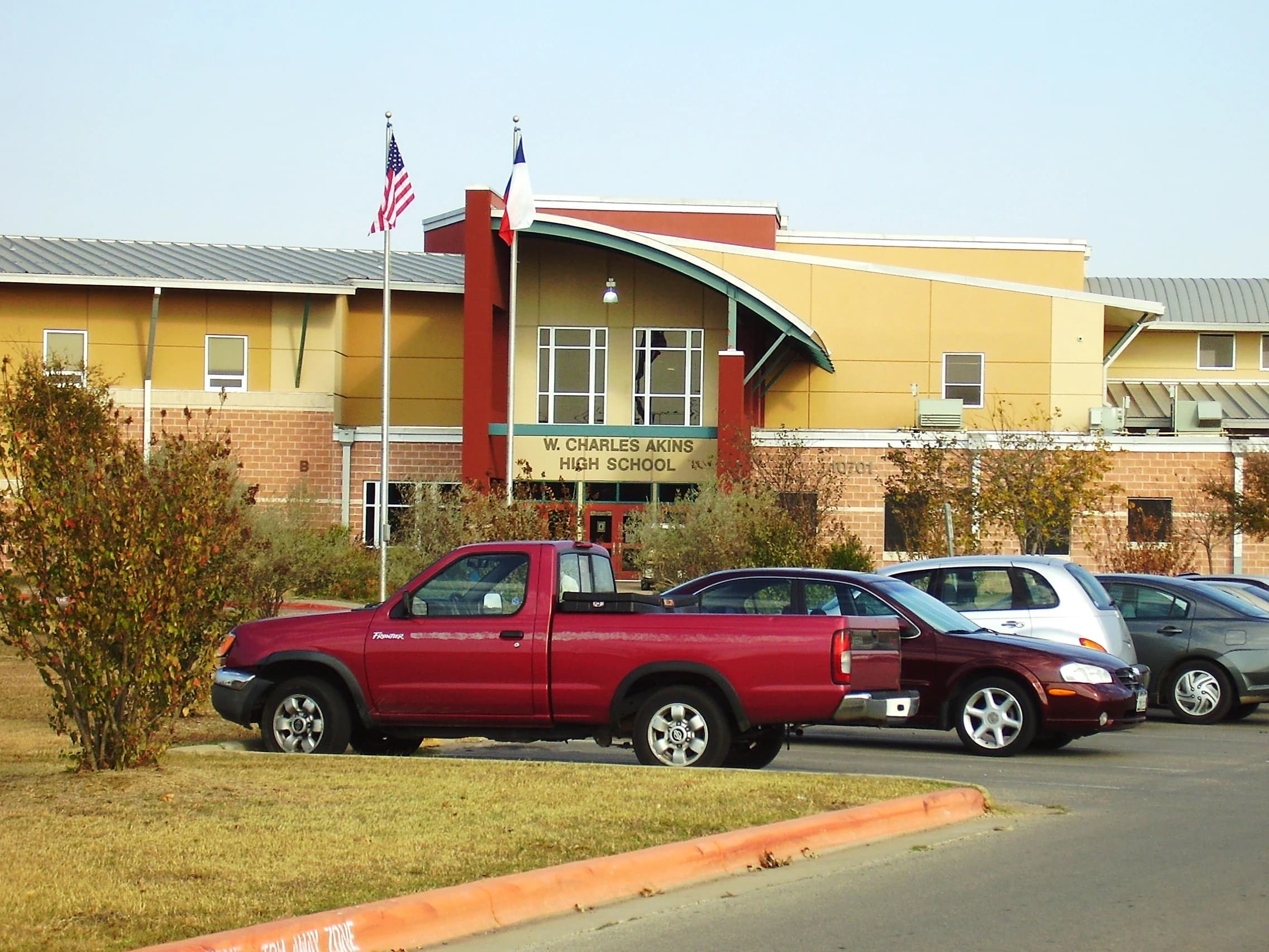 The curved-roof entrance of W. Charles Akins High School in south Austin, with the U.S. and Texas flags out front and cars parked along the drive