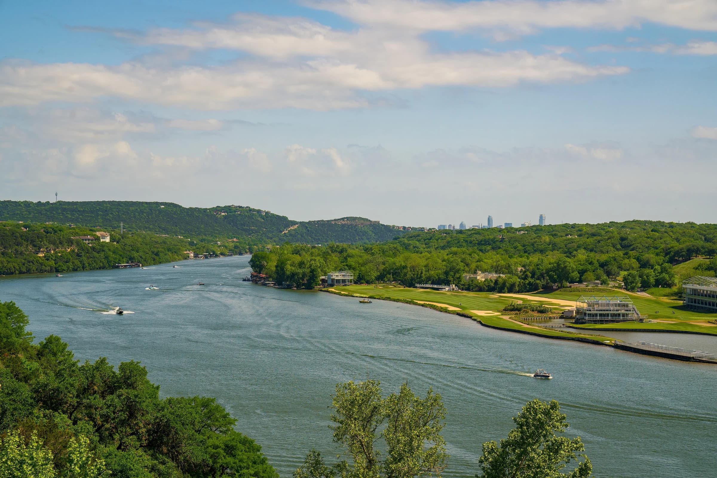 The Colorado River, here Lake Austin, winding between wooded Hill Country ridges toward the distant downtown Austin skyline, seen from the Pennybacker Bridge overlook on Loop 360