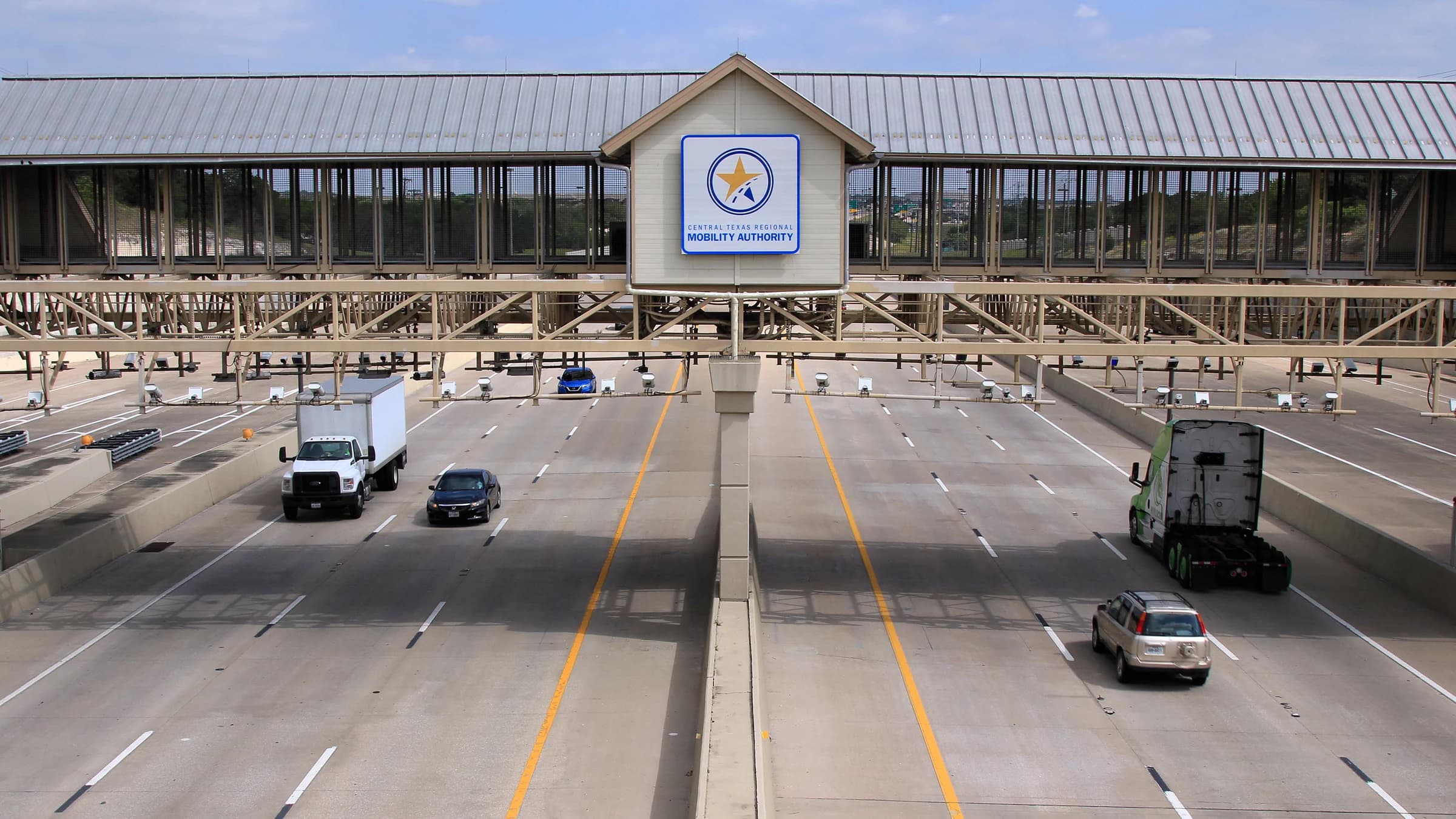 Cars and trucks passing under the steel gantry of the 183A Toll Road mainline toll plaza at Park Street in Cedar Park, on the tolled route between Leander and Austin