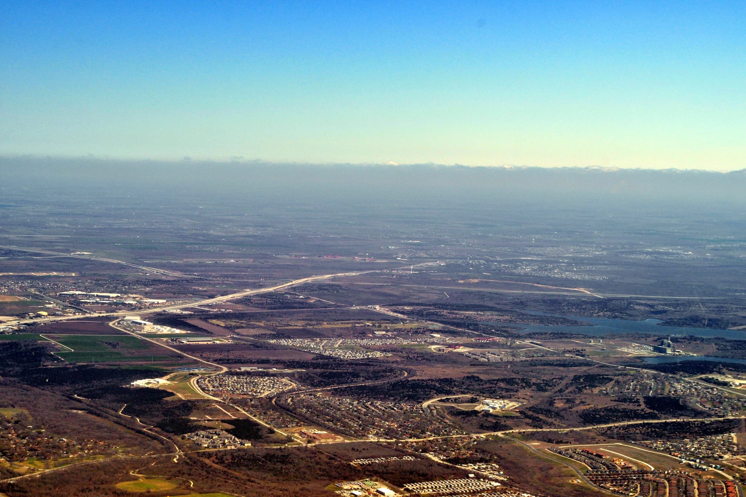 Aerial view looking east-northeast across northeast Austin in March 2015, with Walter E. Long Lake and its power plant at right and open farmland stretching toward Manor under a hazy sky