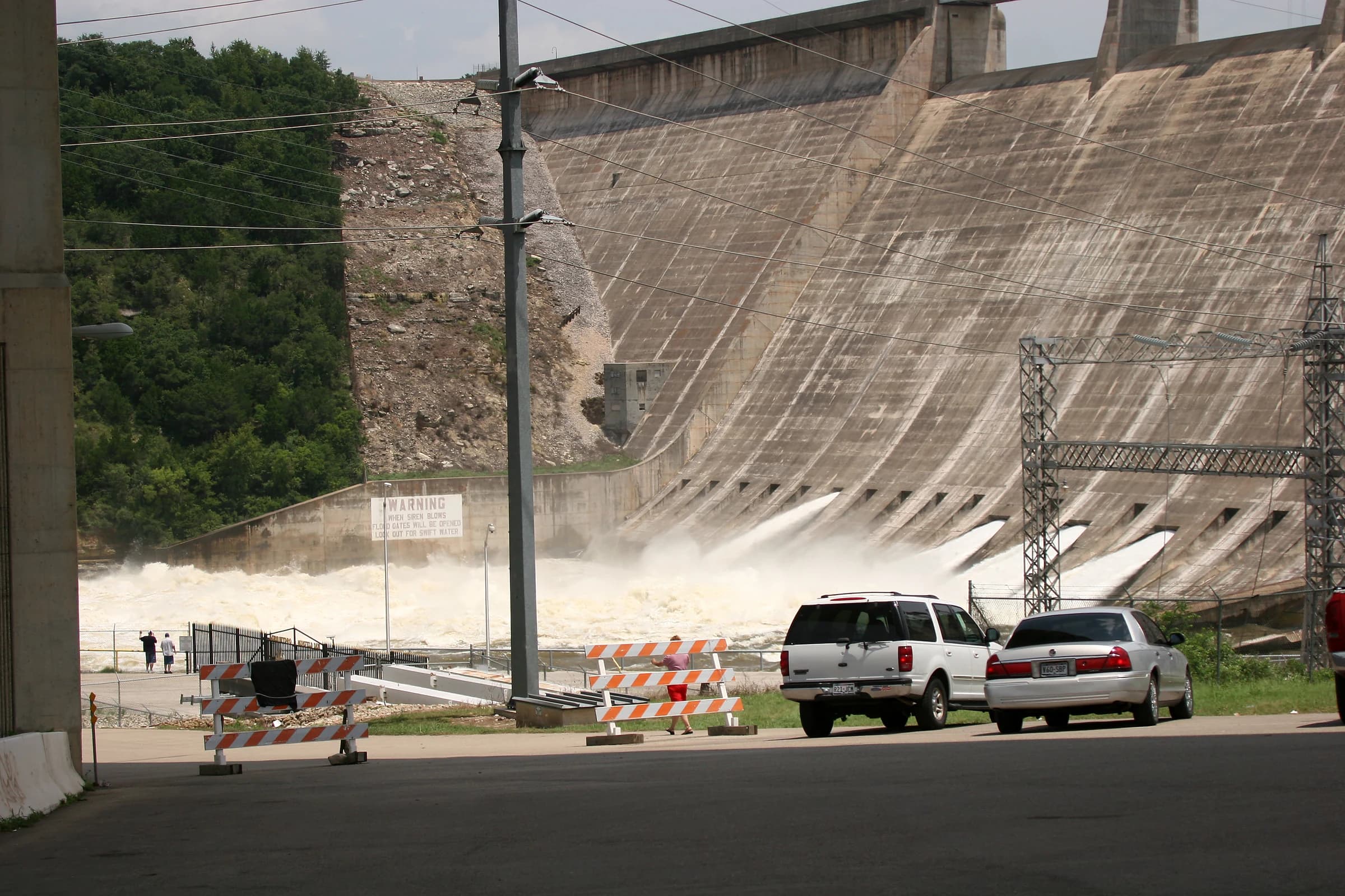 Water pouring from open floodgates at the base of Mansfield Dam on Lake Travis in July 2007, seen from the road below the curved concrete dam face